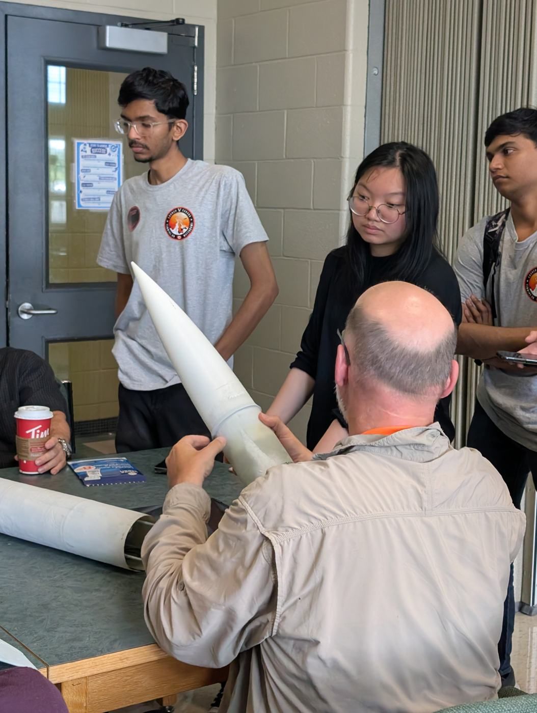 Members watching a mentor examine a rocket nose cone