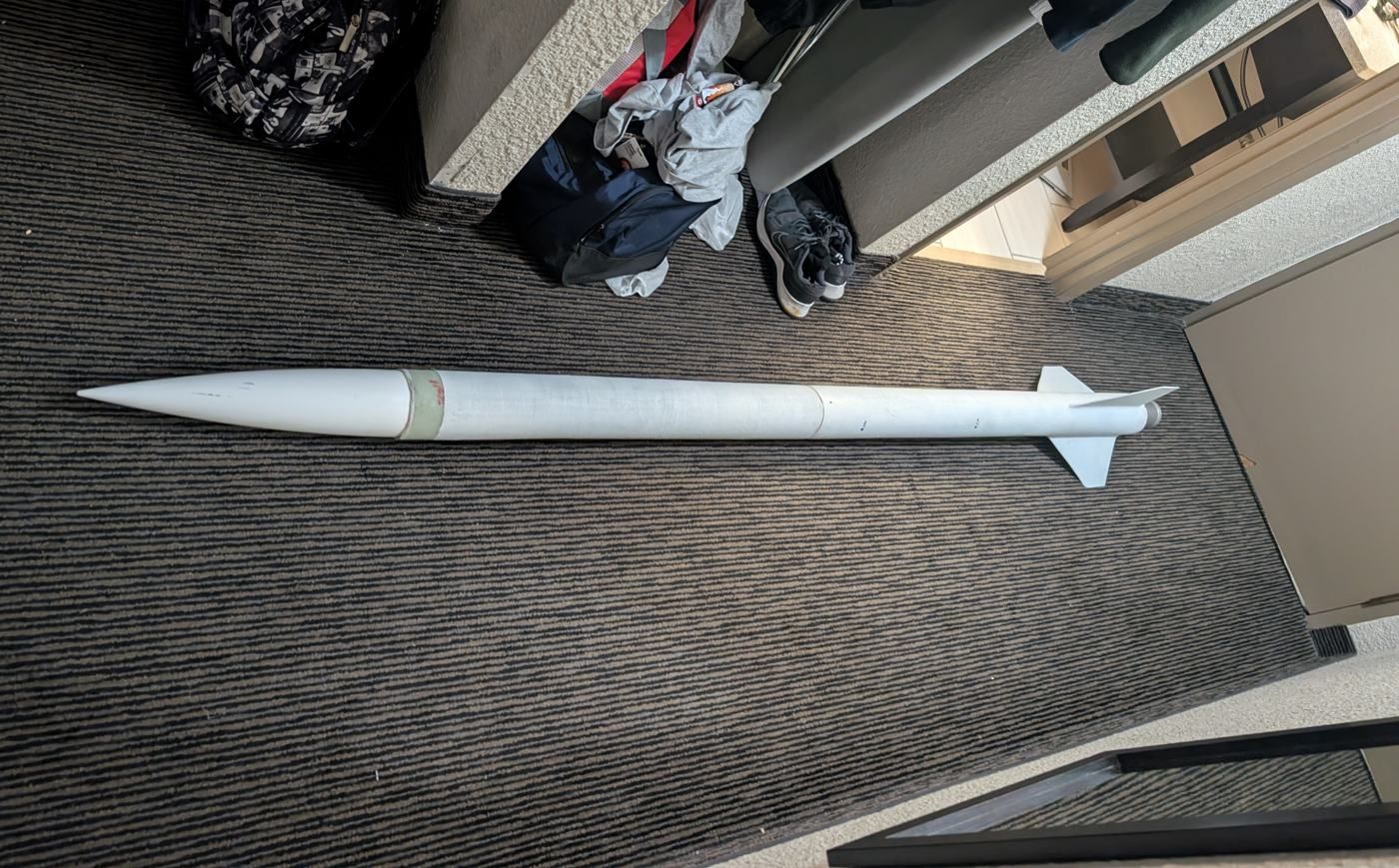 A white rocket laid out on a carpeted floor