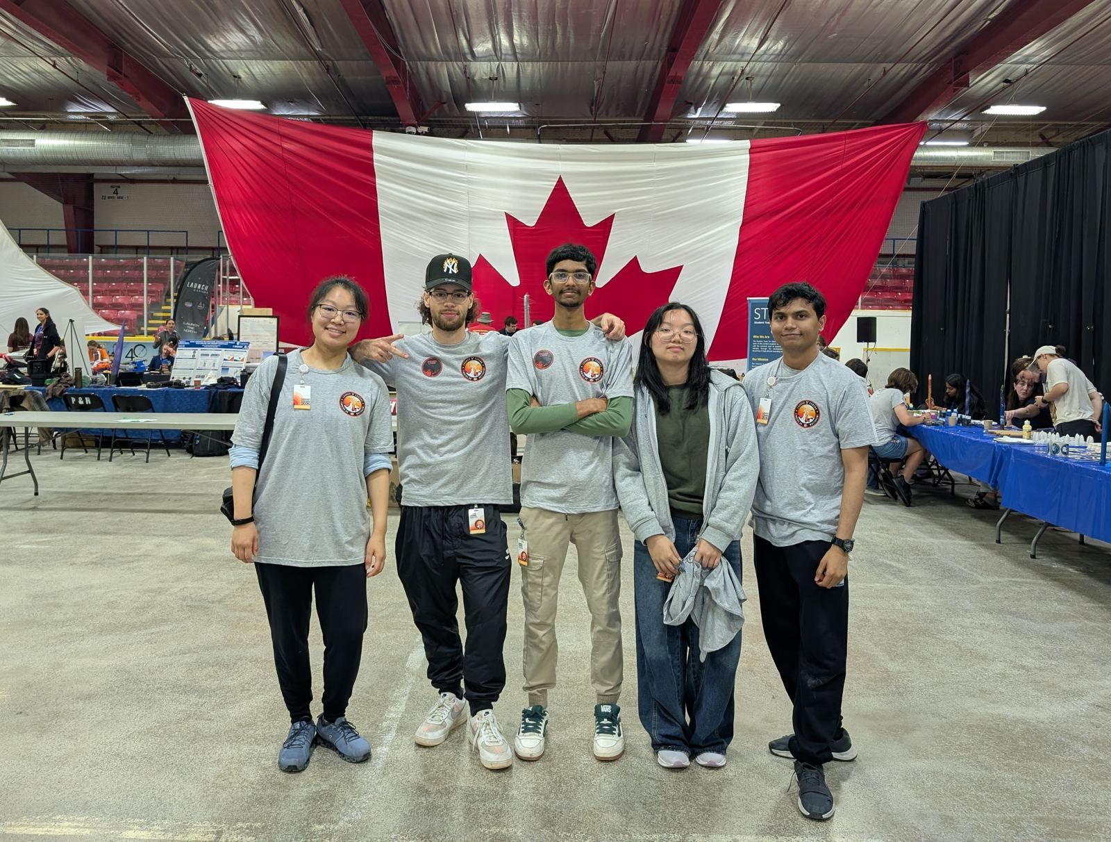Five Astra Labs members in team shirts standing in front of a large Canadian flag at the Launch Canada hall